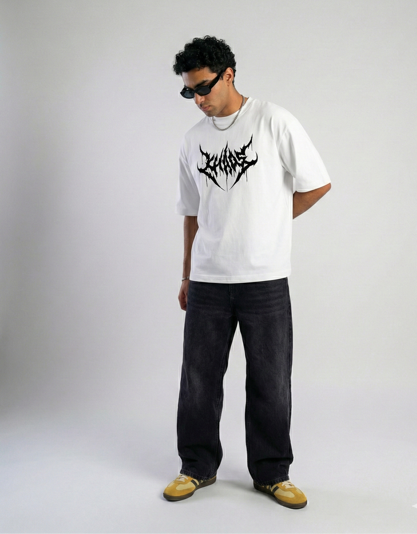 Person wearing a white t-shirt with a black logo and dark jeans on a plain background