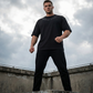 Man wearing a black 'Born of Rage' t-shirt standing on a concrete ledge with a cloudy sky background.
